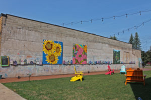 Colorful murals at a local park in Powderhorn Village, with Adirondack chairs on the lawn.