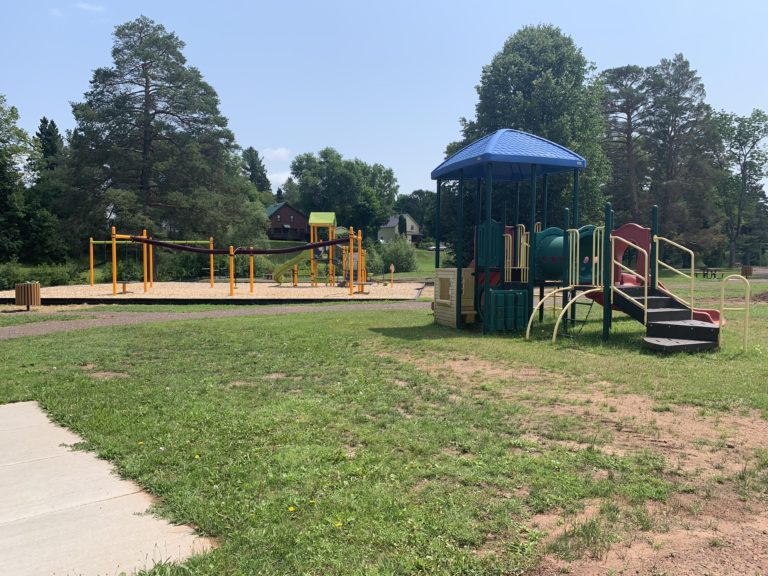 Playground in a local park near Big Powderhorn Mountain, with slides, climbing structures, and green grass.