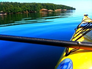 Kayaking on calm blue water near a tree-lined shore, a Powderhorn Village attraction in the Upper Peninsula.