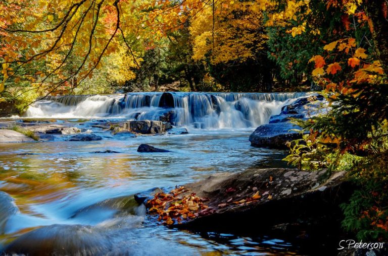 Waterfall cascading over rocks surrounded by fall colors near Big Powderhorn Mountain.