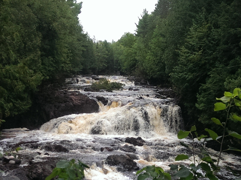 Scenic waterfall cascading over rocks, surrounded by lush trees. Waterfalls near Big Powderhorn Mountain.