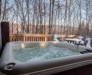 Hot tub on a deck overlooking bare trees, perfect winter lodging near Big Powderhorn Mountain.