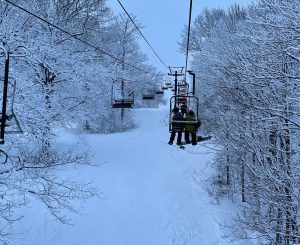 Ski lift at Big Powderhorn Mountain carrying skiers and snowboarders through snow-covered trees. Powderhorn Village skiing.
