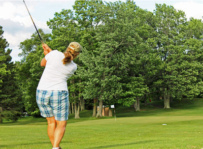 Golfer in plaid shorts swinging club on green; Powderhorn Village attraction.
