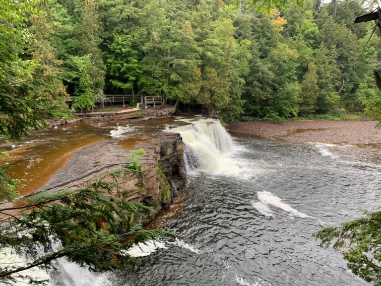 Waterfalls cascade over rocks amidst lush greenery, a scenic Upper Peninsula outdoor adventure.