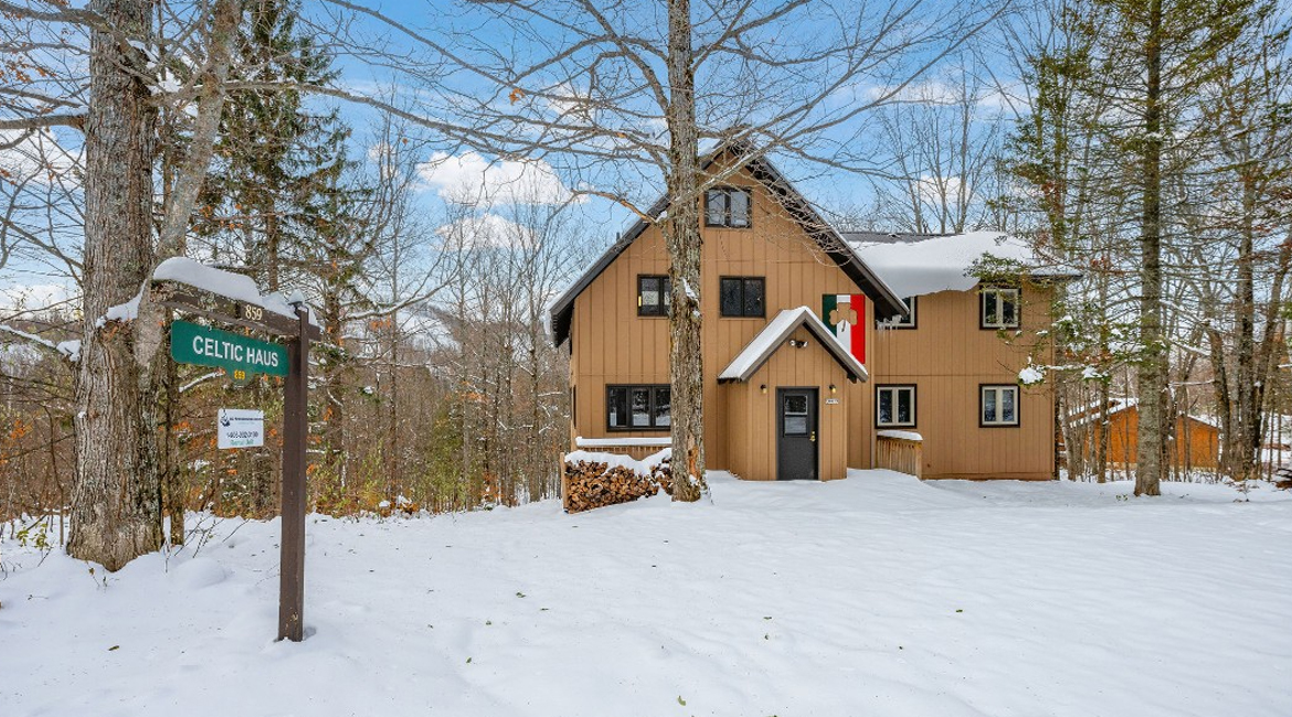 Celtic Haus sign and cozy cabin in a snowy forest setting.