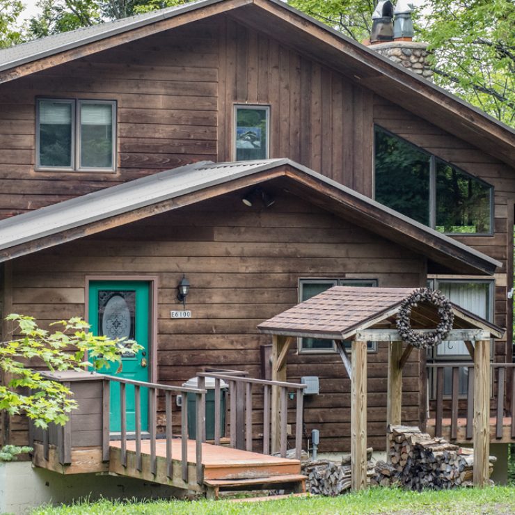 Rustic wooden cabin with a teal door and a small porch in a wooded area.