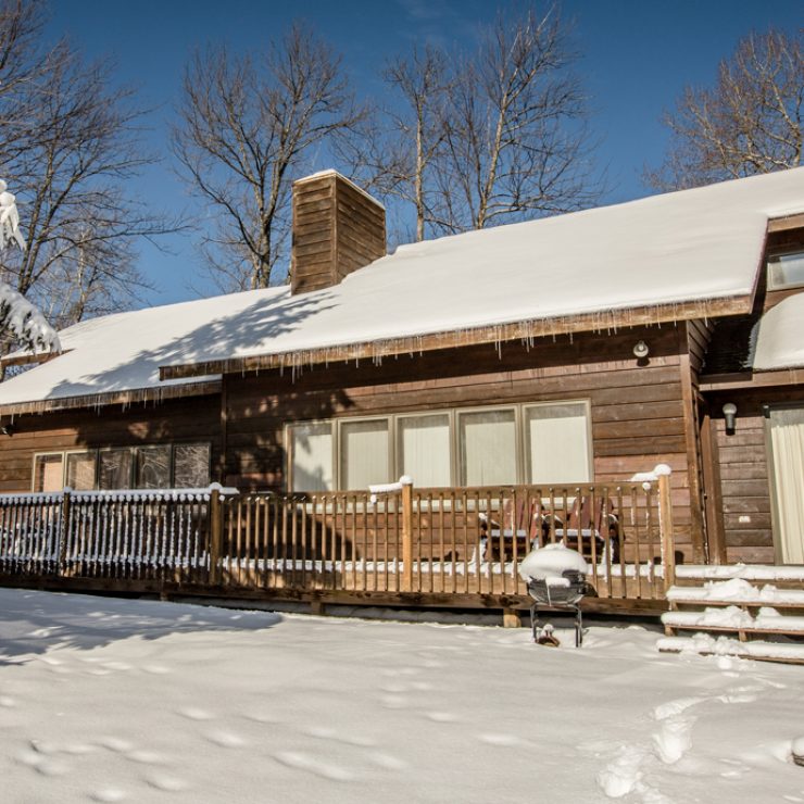 Snowy WINTERPARK cabin with a wooden deck and icicles hanging from the roof on a sunny day.