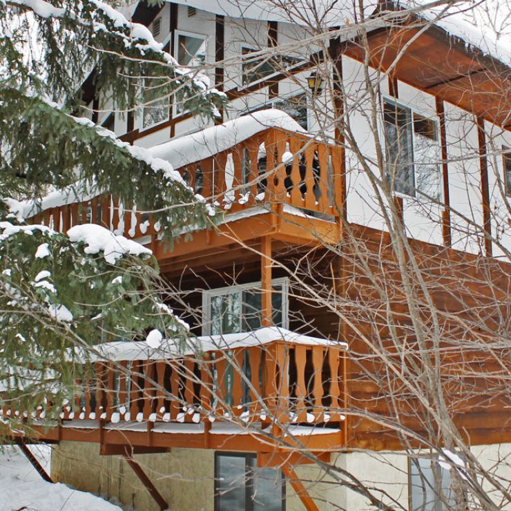 Snowy Holiday Haus with wooden balconies and snow-covered trees, winter scene.