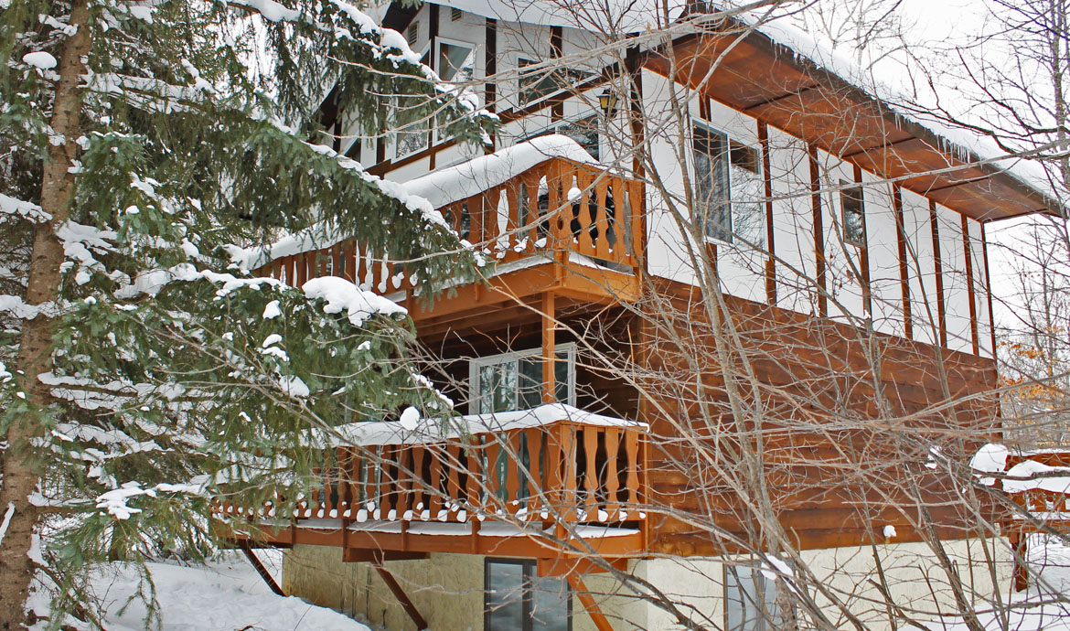 Snowy Holiday Haus with wooden balconies and snow-covered trees, winter scene.