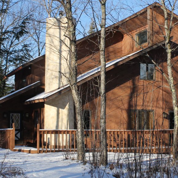 Brown MATTERHORN cabin with a stone chimney and snow-covered ground surrounded by bare trees.
