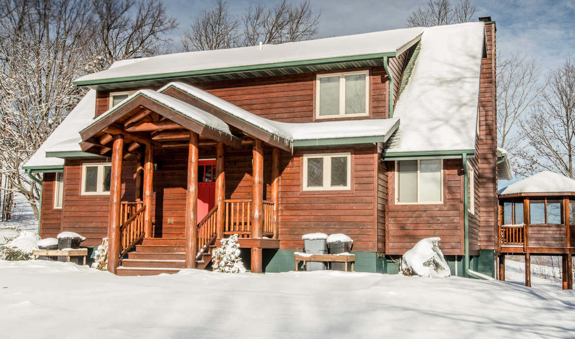 SNO SUMMIT: Cozy cabin covered in snow with a red door and log porch.