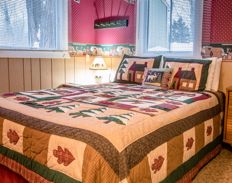 Cozy bedroom with a patchwork quilt featuring bear and cabin motifs, fitting for a "Bear Hug" themed blog.