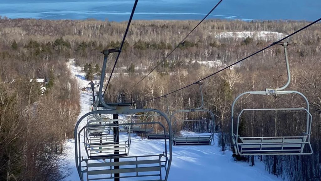 Ski lift ascending a snowy hill with trees and a lake in the background, near Big Powderhorn Lodging.