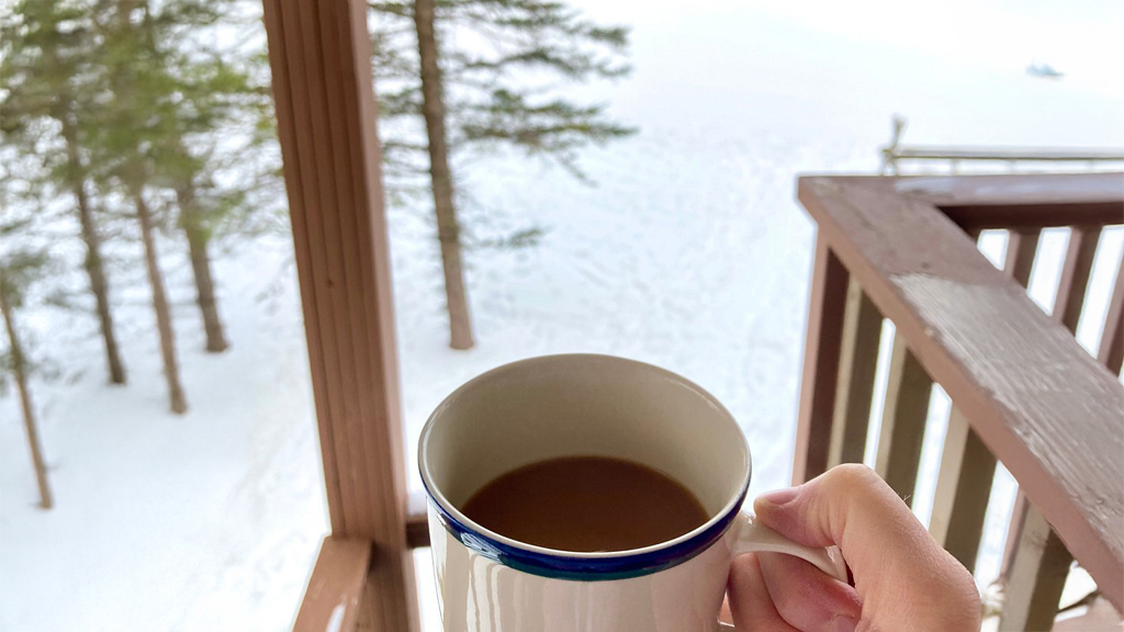 Cozy coffee mug on a Big Powderhorn Lodging winter balcony overlooking snowy trees