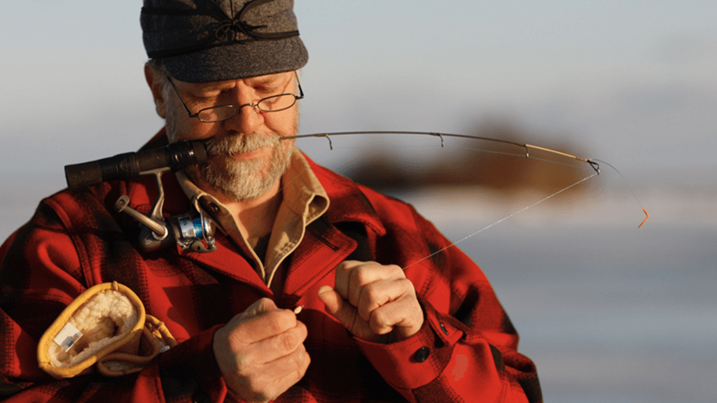 Man ice fishing in Upper Peninsula winter activities, holding rod in mouth.