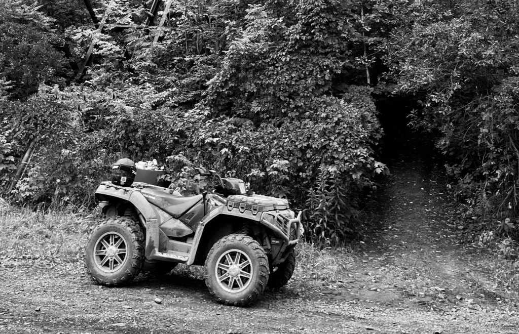 ATV parked on a dirt trail near trees, ideal for ATV and snowmobile trails in Powderhorn Village.